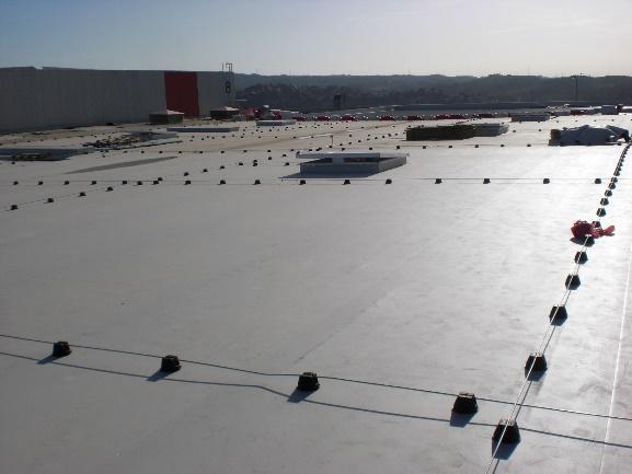 Amplia perspectiva de una azotea comercial o industrial, con una superficie de membrana clara y un sistema de línea de vida horizontal de gran envergadura para la seguridad en trabajos en altura.