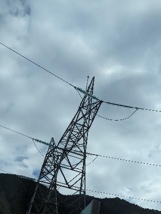 Vista desde abajo de una torre de tendido eléctrico de alta tensión, con sus cables y aisladores, silueteada contra un cielo con nubes dispersas.
