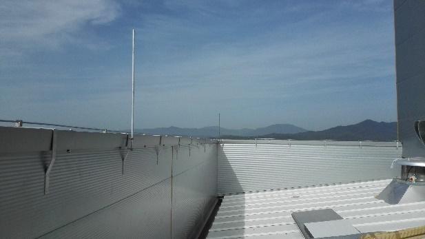 Perspectiva de una azotea industrial equipada con una barandilla de seguridad metálica y un pararrayos, con cadenas montañosas en el horizonte bajo un cielo despejado.