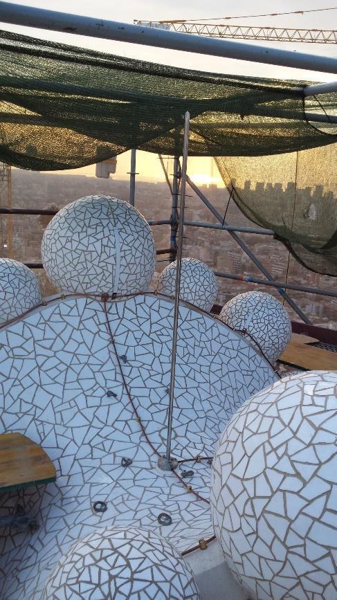 Primer plano de las esferas y superficies curvas cubiertas de trencadís en una de las torres de la Sagrada Familia, con el horizonte de la ciudad visible al fondo.