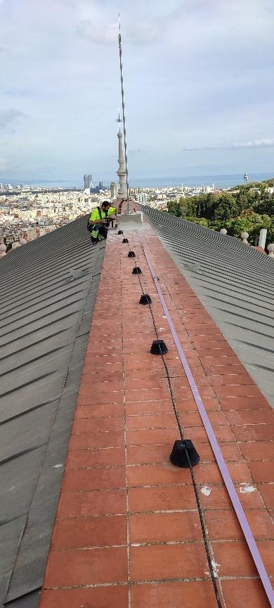 Un operario realizando tareas de mantenimiento en la cumbrera de un tejado, con vistas a la ciudad.