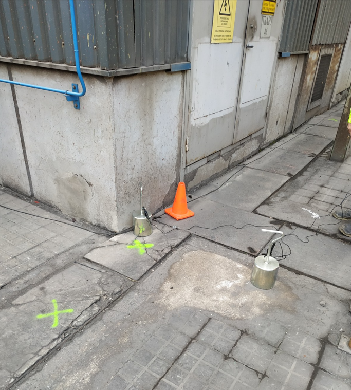 Equipos de medición en el suelo junto a subestación eléctrica, con señalización de advertencia visible.