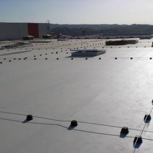 Amplia perspectiva de una azotea comercial o industrial, con una superficie de membrana clara y un sistema de línea de vida horizontal de gran envergadura para la seguridad en trabajos en altura.