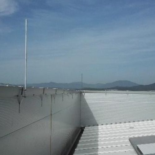 Perspectiva de una azotea industrial equipada con una barandilla de seguridad metálica y un pararrayos, con cadenas montañosas en el horizonte bajo un cielo despejado.