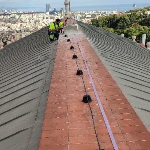 Un operario realizando tareas de mantenimiento en la cumbrera de un tejado, con vistas a la ciudad.